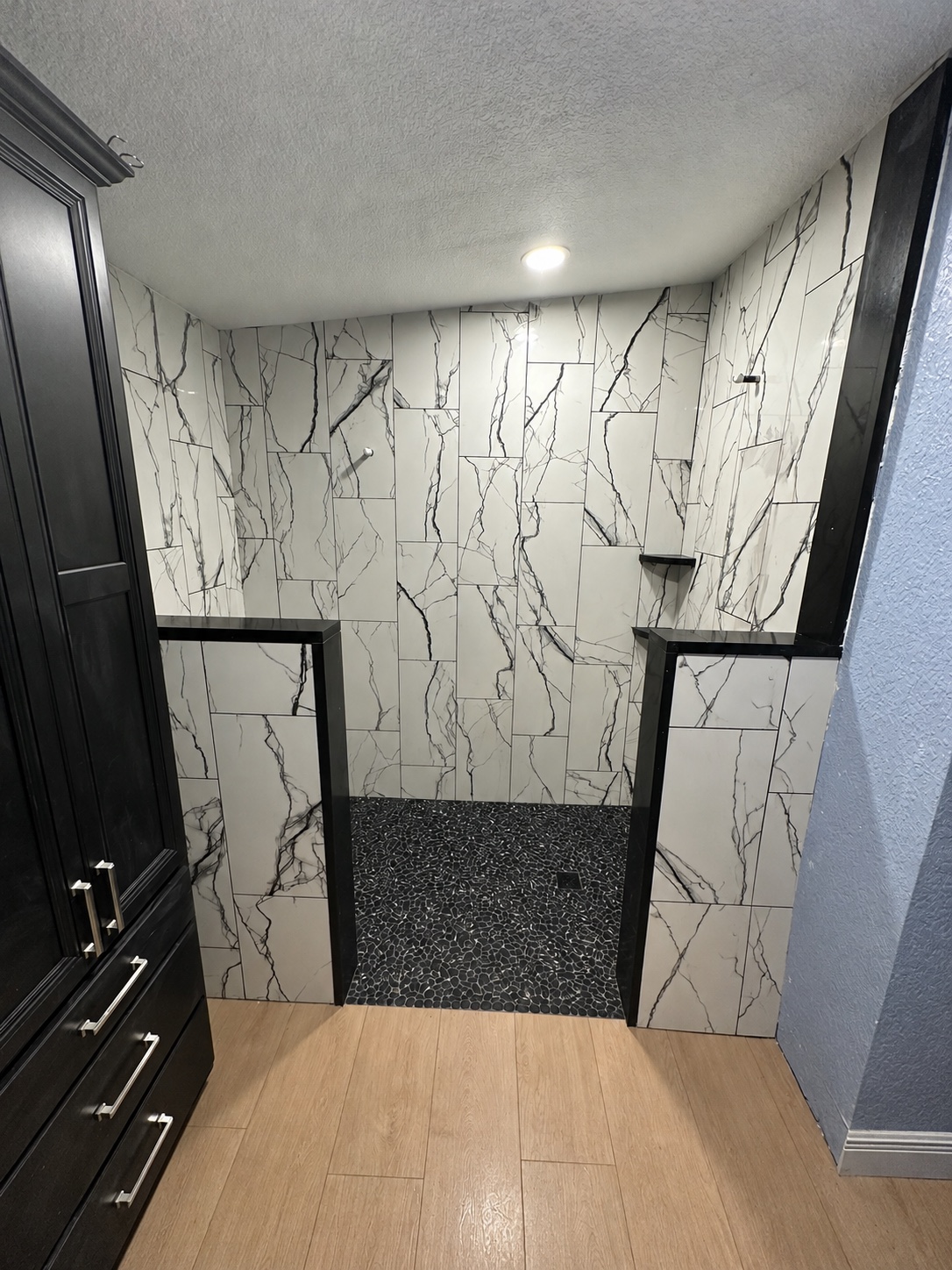 White shower wall tile with bold black veining and a black pebble floor during installation