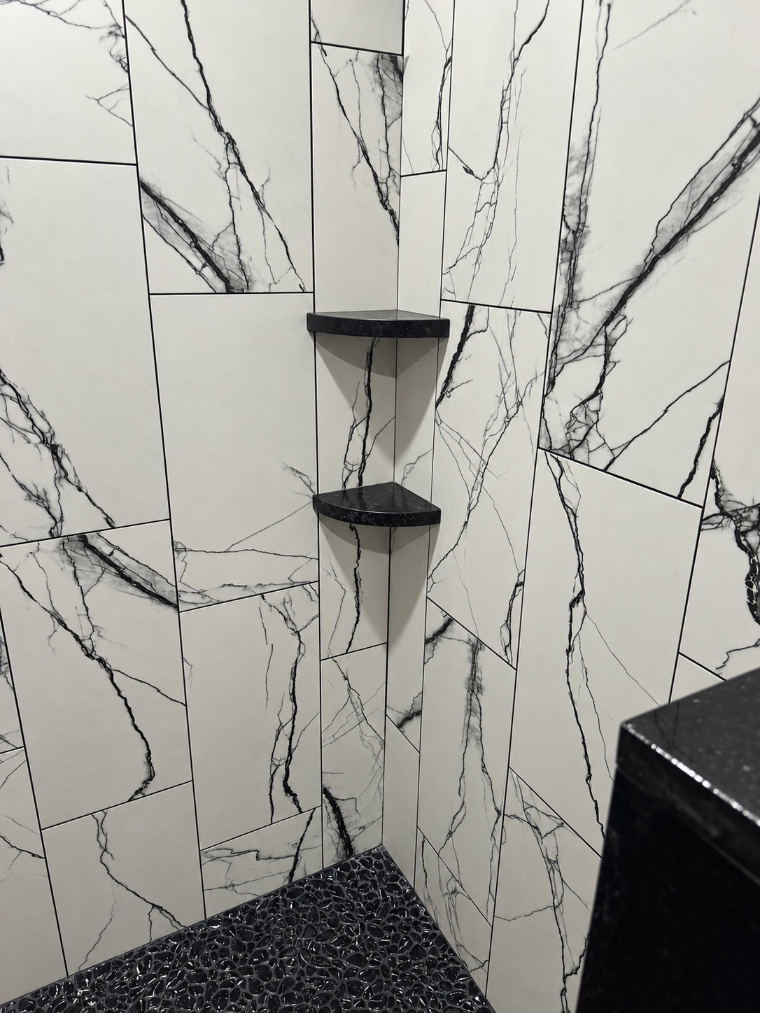 Black corner shelves against white shower tile with black veining during installation