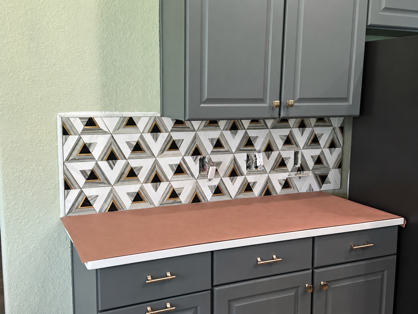 Black, white, gray and gold geometric kitchen backsplash during installation