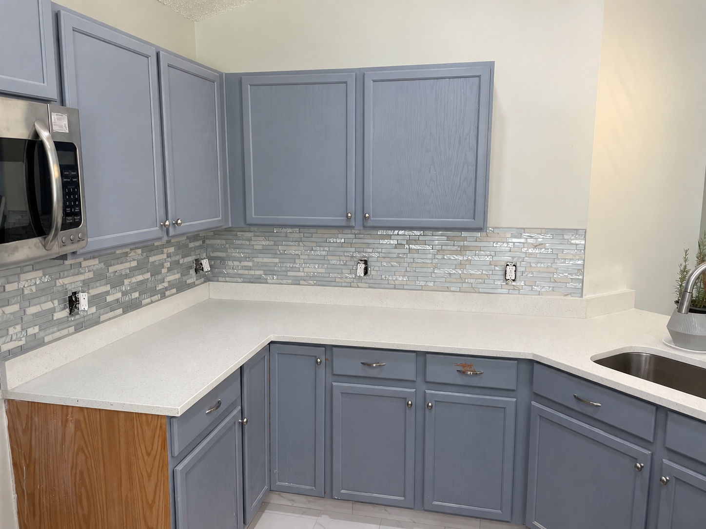 Pale glass mosaic kitchen backsplash with blue-gray cabinets during installation
