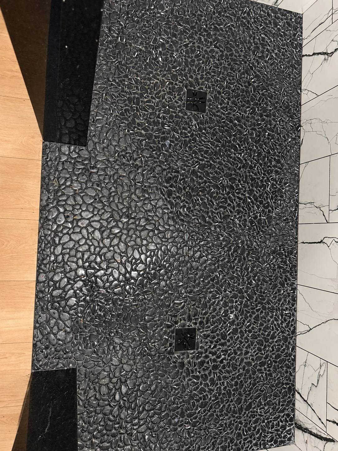 Black pebble shower floor with two square drains during installation
