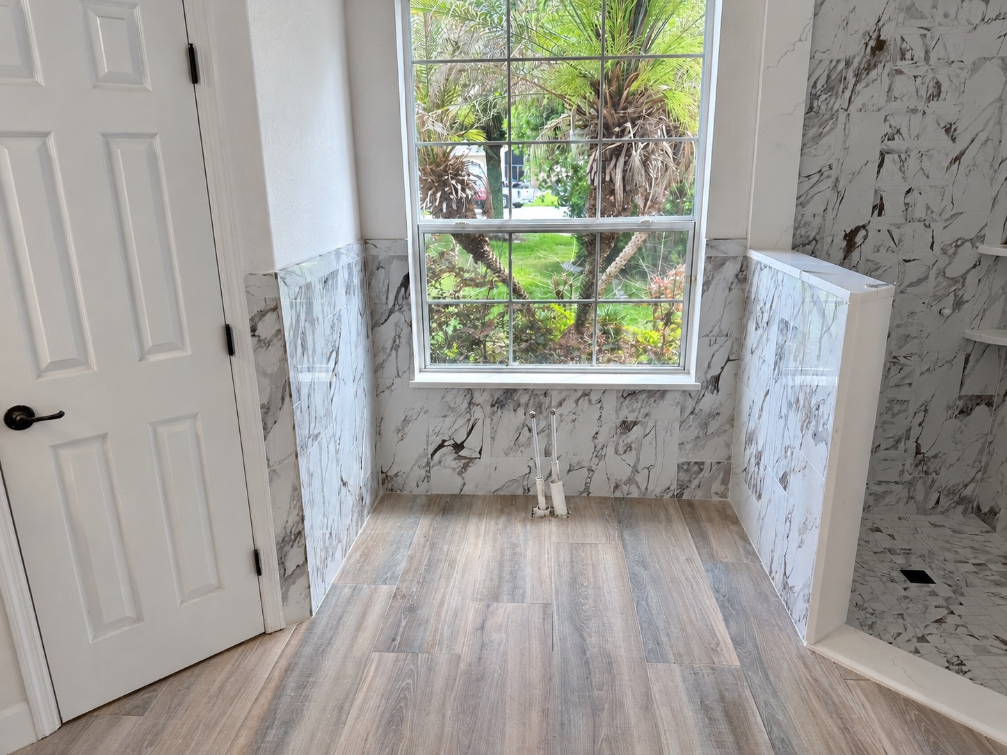Wood-look bathroom floor and marble-look wall tile around a bright window during installation